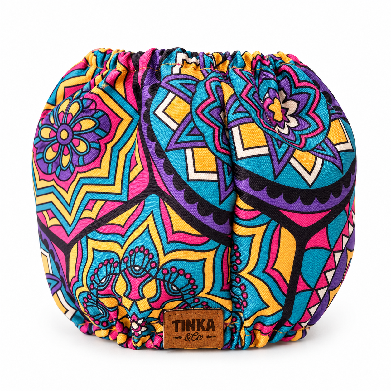 A round, drawstring-style pouch or bag with a vibrant, multicolored mandala and geometric pattern in pink, blue, yellow, purple, and black. A brown leather brand patch reading 'TINKA & Co' is sewn onto the front.