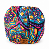 A round, drawstring-style pouch or bag with a vibrant, multicolored mandala and geometric pattern in pink, blue, yellow, purple, and black. A brown leather brand patch reading 'TINKA & Co' is sewn onto the front.