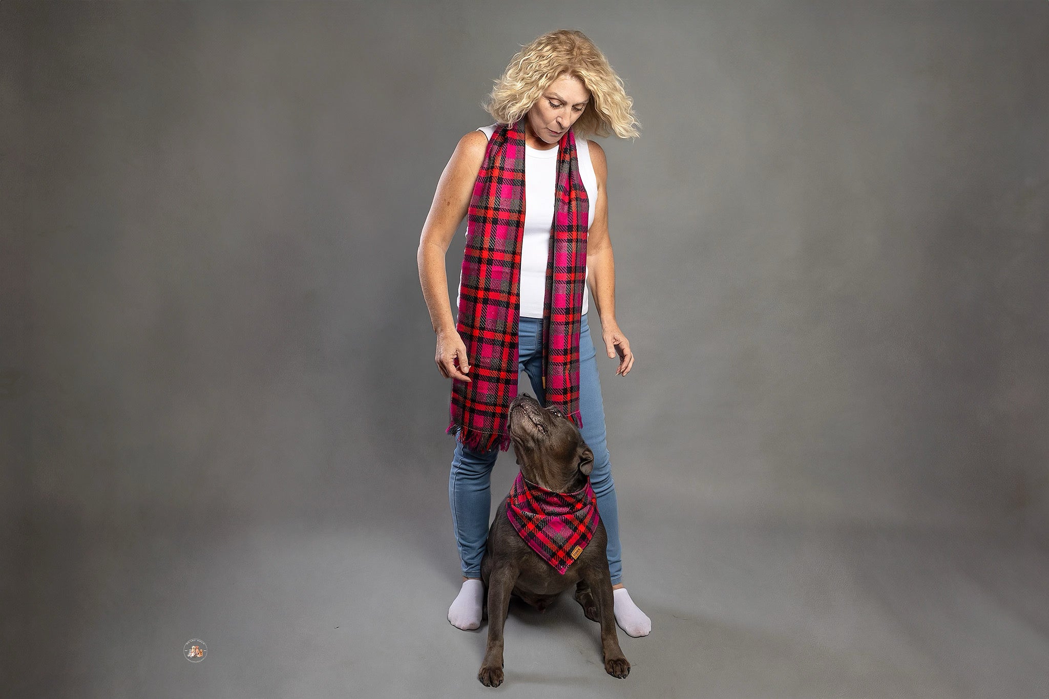 A person standing with a black dog in front of them, both wearing matching pink plaid scarves.