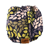A pair of ruffled bloomers with a navy blue background and a retro leaf pattern in olive green, light pink, and gray. A brown leather patch on the front reads 'TINKA & CO'