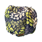 A reusable fabric diaper cover by TINKA & CO, featuring a navy blue background with a pattern of olive green, lime green, and cream leaf shapes. The brand name 'TINKA & CO' is visible on a small brown label at the bottom edge.