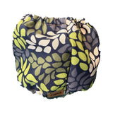 A reusable fabric diaper cover by TINKA & CO, featuring a navy blue background with a pattern of olive green, lime green, and cream leaf shapes. The brand name 'TINKA & CO' is visible on a small brown label at the bottom edge.