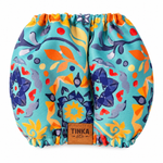 Dog Snood from Tinka & Co, featuring a vibrant, multicolor abstract floral and leaf pattern on a turquoise background, with a brown leather brand patch at the bottom center.